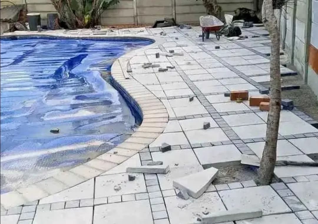 Pool surround being paved in light-coloured slabs
