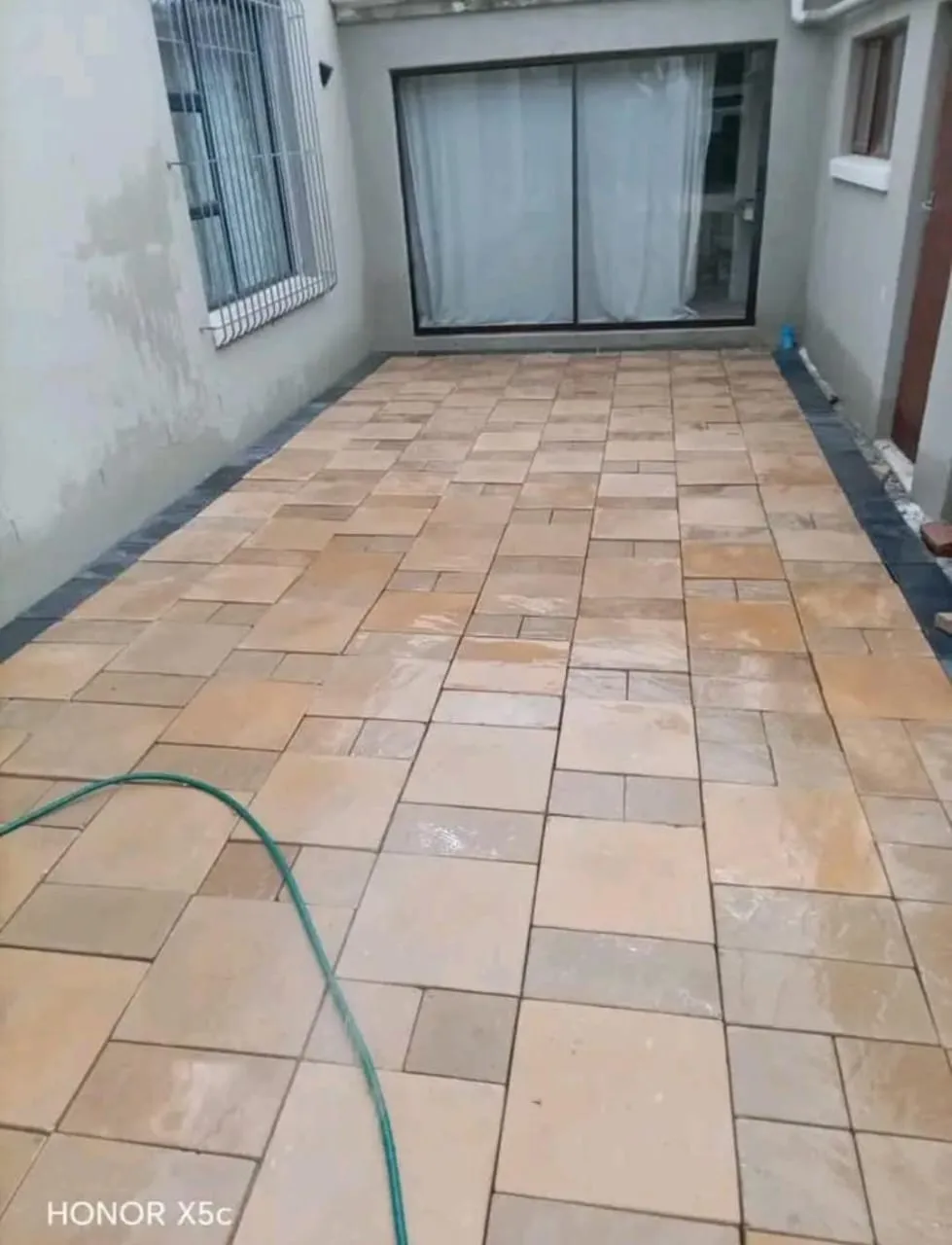 Patio paved in mixed-size sandstone-coloured pavers