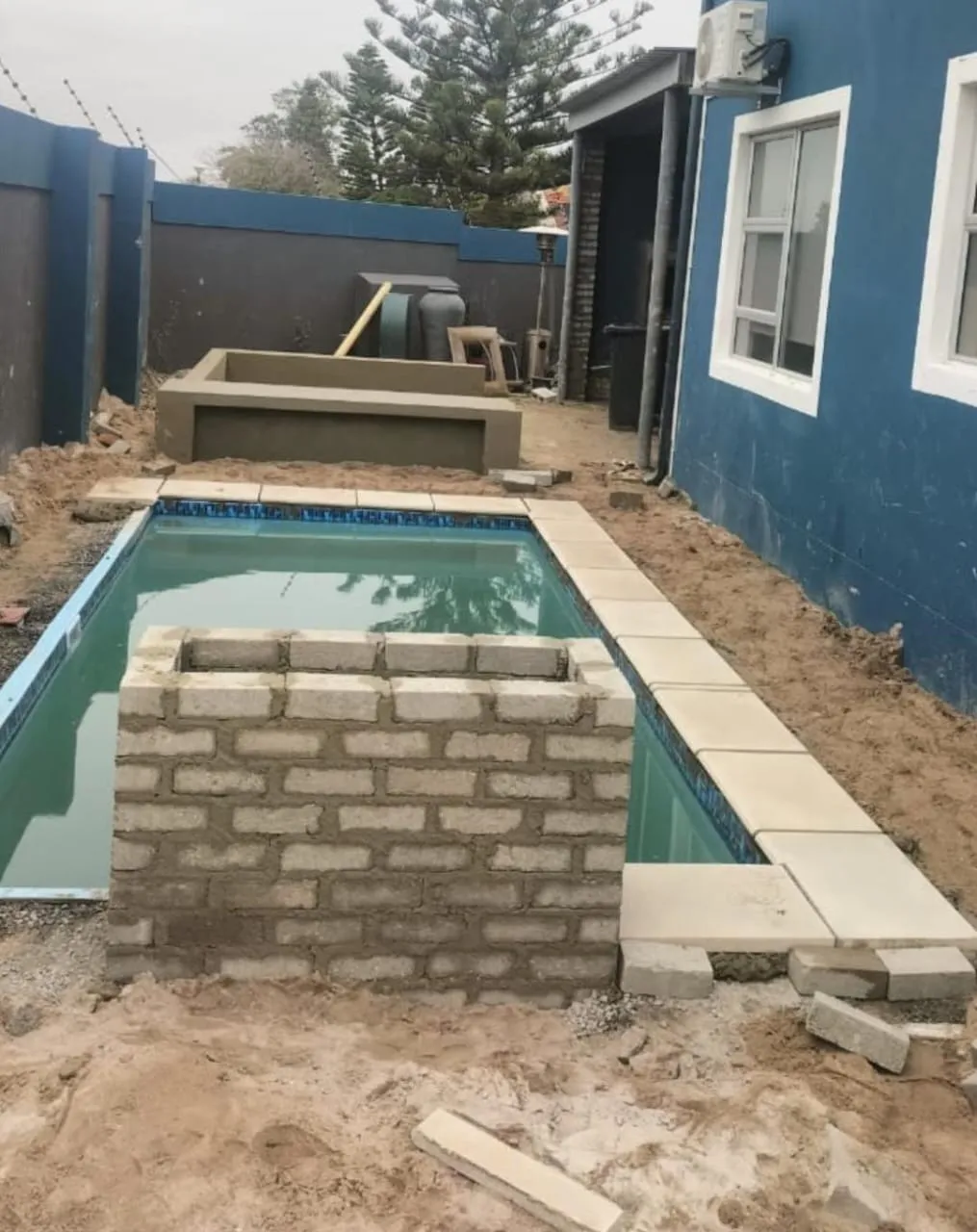 Plunge pool with paving and a stone-clad feature wall under construction